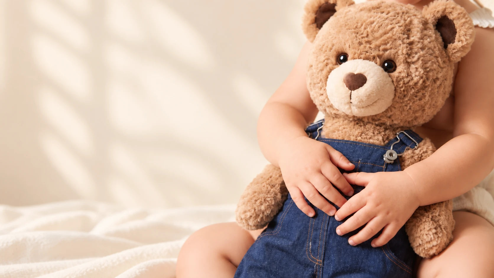 A child hugging a plush bear dressed in denim overalls